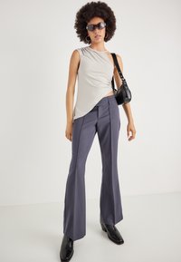 Canotta grigio chiaro senza maniche con design asimmetrico; pantaloni a campana blu navy; borsa nera; stivaletti neri lucidi alla caviglia; occhiali da sole.