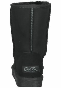 Botines de ante negro con un acabado ligeramente texturizado, que presentan costuras laterales, una suela plana y un parche con logo en la parte posterior.
