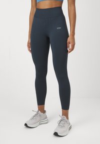 Magas derekú, sötétkék leggings nyújtható anyagból, sima textúrával. A derékrészen logó található, valamint formázó varrási részletek.