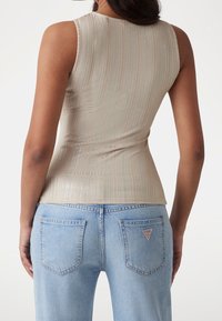 Top senza maniche a coste beige realizzato in tessuto lucido, design aderente. Abbinato a jeans in denim azzurro chiaro con un logo triangolare sulla tasca posteriore.