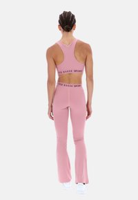 Różowy sportowy top crop oraz dzwony leggingi wykonane z elastycznego materiału, z czarną taśmą z logo "TED BAKER SPORT" w talii.