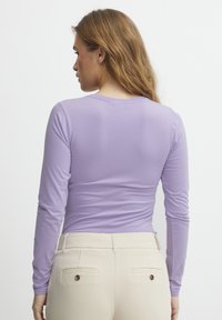 Lange mouwen lilakleurig top van een soepele stof, geschikt ontwerp, met een ronde hals. In combinatie met beige broek met twee achterzakken en knopen.