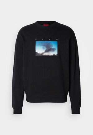 Juodas džemperis su grafikiniu spausdiniu, vaizduojančiu paukščius skraidančius mėlynajame danguje. Apvalus kaklas, gumuoti rankogaliai ir apačia. Prekės ženklas "Hugo" virš paveikslėlio.