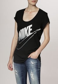 Svart bomullströja med vid halsringning och uppvikta korta ärmar, med en stor silverfärgad Nike-logotyp och en böjd swoosh-design.