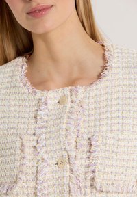 Tweed jack met zachte pastelkleuren, rafelige randen, ronde halslijn en twee voorzakken. Voorzien van lichtbeige knopen voor sluiting.