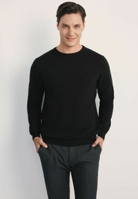 Czarny sweter dzianinowy z okrągłym dekoltem, w połączeniu z ciemnoszarymi spodniami. Tkanina wydaje się gładka, bez wzorów ani widocznych akcentów.