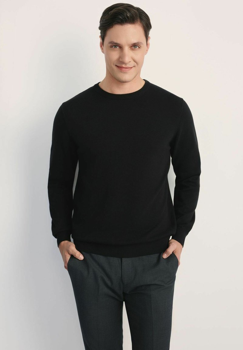 Czarny sweter dzianinowy z okrągłym dekoltem, w połączeniu z ciemnoszarymi spodniami. Tkanina wydaje się gładka, bez wzorów ani widocznych akcentów.