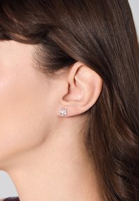 Kolczyk w kształcie płatka śniegu, zdobiony diamentami, w srebrnym odcieniu, z misternie wykonanymi detalami i wypolerowanym wykończeniem, zaprezentowany na uchu modelki.