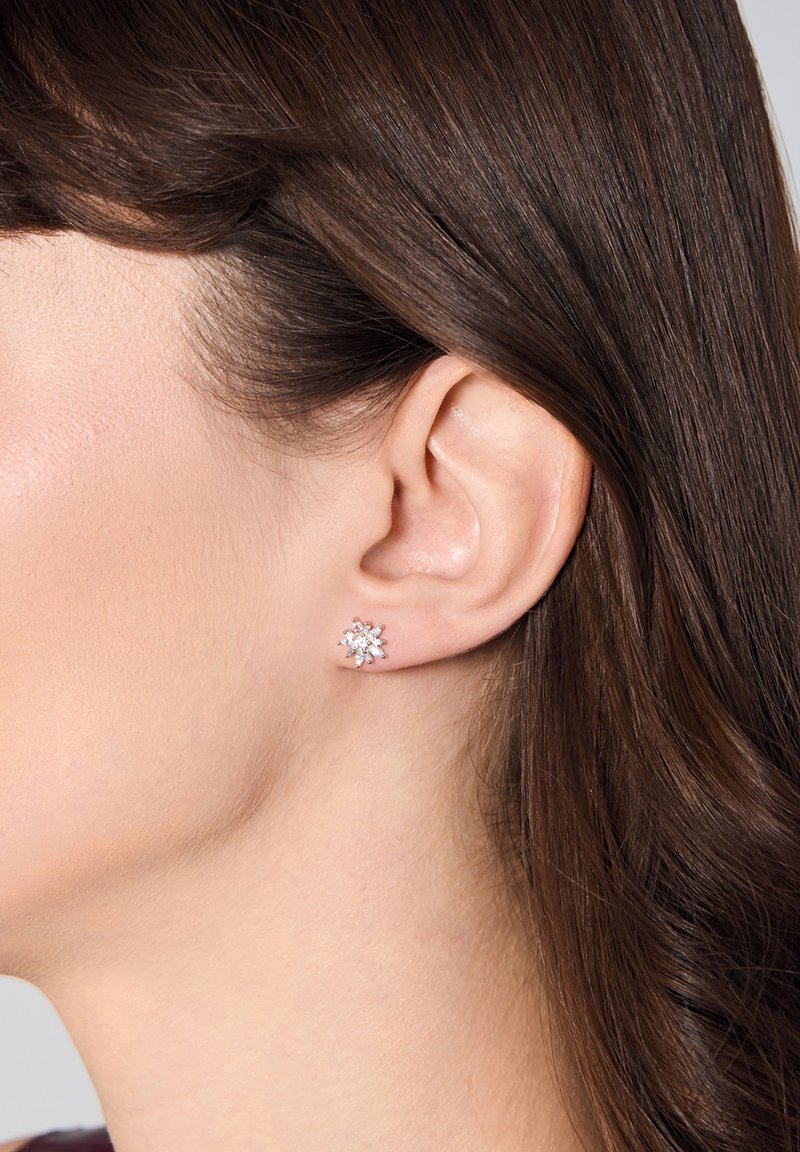 Kolczyk w kształcie płatka śniegu, zdobiony diamentami, w srebrnym odcieniu, z misternie wykonanymi detalami i wypolerowanym wykończeniem, zaprezentowany na uchu modelki.