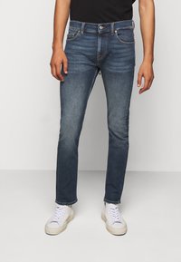 Tmavě modré džíny ve slim fit, s pěti kapsami, knoflíkovým zapínáním a jemným blednutím na stehnech. Kombinované s bílými teniskami.