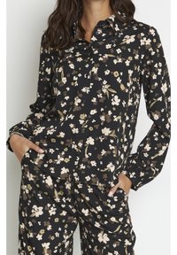 Czarna koszula zapinana na guziki w kwiaty z kremowymi i oliwkowymi kwiatami, długimi rękawami oraz luźnym krojem i kołnierzykiem z ostrym zakończeniem.