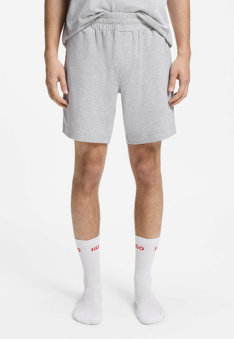 Homme portant un short gris clair à taille élastique et des chaussettes blanches de marque HUGO, debout les mains détendues sur les côtés.