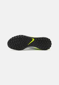 Schwarze Gummisohle mit strukturiertem Muster und einem auffälligen gelben Nike-Logo; zeichnet sich durch ein elegantes graues Oberdesign mit grünen Akzenten aus.