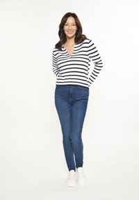 Csíkos fekete-fehér pulóver V-nyakkal, sötétkék skinny farmerral és fehér sportcipővel párosítva. Sima textúra és testhezálló kialakítás.