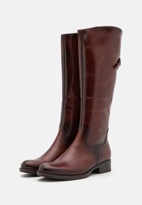 Botas de cuero marrón hasta la rodilla con una textura suave, puntera redonda y tacón bajo en bloque; cuentan con una correa decorativa en el lateral.