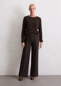 Pull en maille marron associé à un pantalon marron taille haute et à jambes larges. Le modèle porte des talons marron sur un fond neutre.