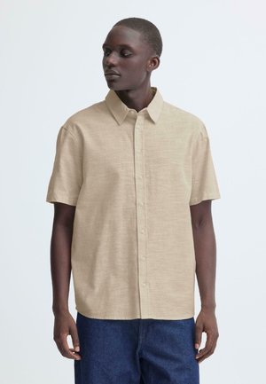 Beiges Kurzarmhemd mit Knöpfen aus strukturiertem Stoff, mit klassischem Kragen und geradem Saum, kombiniert mit dunklen Jeans.
