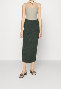 Knit midi-hame tummanvihreässä ribbitekstuuri, yhdistettynä vaaleanharmaaseen hihattomaan puseroon. Mallilla on päällään harmaat mulesit, joissa on neliömäinen varvas ja solki.