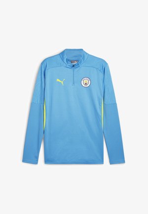 Ljusblå långärmad sporttröja med halvlång dragkedja, gula accenter, texturerat tyg och Manchester City-logotypen på bröstet.