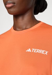 Oranž lühikeste varrukatega T-särk sujuvast materjalist, millel on rinna peal valge "TERREX" logo ja klassikaline ümar kaelus.