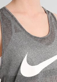 Šedý sportovní tílko s texturovaným vzorem, na přední straně s bílým logem Nike. Kulatý výstřih a bez rukávů.