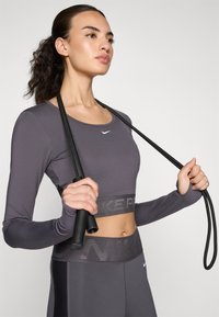 Gray long-sleeve crop top with a small white logo, paired with high-waisted leggings featuring a textured waistband and a jump rope.