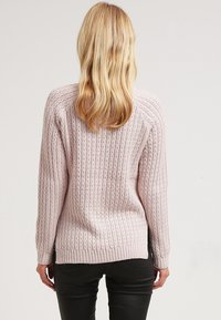 Ljusrosa stickad tröja med ett texturerat mönster, långa ärmar och ribbad nederkant. Bakifrån visas en avslappnad passform och subtila detaljer.