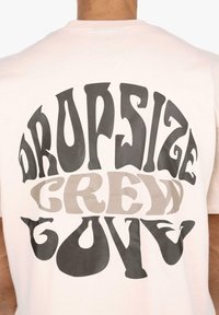 Hellrosa Baumwoll-T-Shirt mit Rundhalsausschnitt, auf dem Rücken mit fett gedrucktem, stilisiertem Text in Schwarz und Grau: "DROPSIZE CREW GUY".