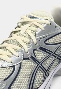 Αθλητικό παπούτσι τρεξίματος με επάνω μέρος από πλέγμα σε άσπρο και ασημί, με μπλε λεπτομέρειες, κρέμα κορδόνια και σχέδιο με ενισχυμένη σόλα.