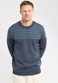 Pull en tricot bleu marine avec une section supérieure à motifs, un col rond et des boutons décoratifs sur l'épaule gauche. Design texturé sur l'ensemble.