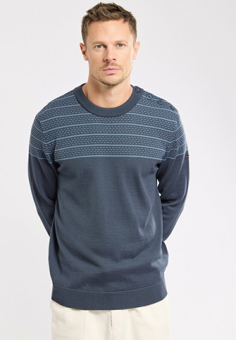 Pull en tricot bleu marine avec une section supérieure à motifs, un col rond et des boutons décoratifs sur l'épaule gauche. Design texturé sur l'ensemble.