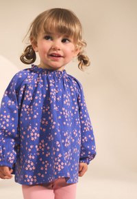 Top a fantasia floreale blu con maniche a sbuffo e scollatura arricciata, abbinato a pantaloni a coste rosa chiaro. Tessuto morbido e strutturato.