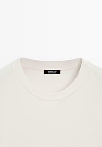 T-shirt blanc à col rond avec col côtelé et étiquette noire portant l'inscription "Massimo Dutti Made in Portugal" à l'intérieur, au niveau de la nuque.