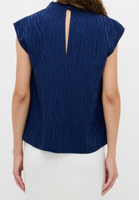 Blusa blu navy con un motivo a zebra testurizzato, maniche corte e un'apertura a chiave sul retro. Tessuto morbido con una vestibilità comoda.