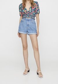 Blouse courte à motifs floraux avec des manches bouffantes, associée à un short en jean à ourlets retroussés et taille haute. Sandales à talons blanches.