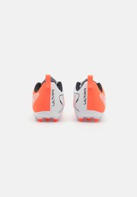 Oranžas un baltas futbola zābaki ar elegantu dizainu, teksturētu virsmu, papēža cilpu un sešiem redzamiem nagiem uz apakšējās daļas.