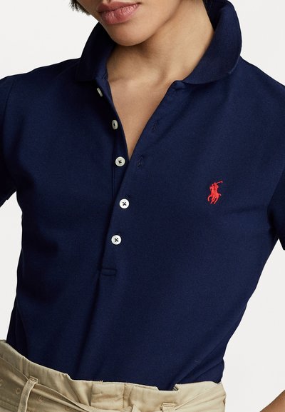 Tamsiai mėlyna polo marškinėliai, pagaminti iš tekstūruoto audinio, su klasikiniu apykakle, trimis mygtukais ir mažuoju raudonu arkliu logotipu kairiajame krūtinės kampe.