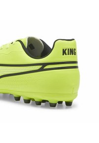 Botas de fútbol de color amarillo brillante con un upper sintético texturizado, detalles en negro, tacos moldeados y un collar de malla para mayor transpirabilidad.