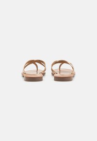 Sandali in pelle marrone con design a strap minimalista e suole piatte, caratterizzati da una texture liscia e punta aperta.