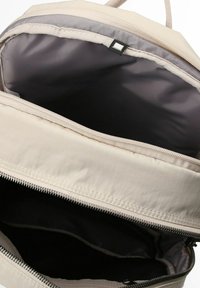 Mochila de color beige claro con apertura con cremallera, con una textura suave y un interior gris. Incluye un bolsillo interior para una mejor organización.