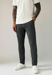Sivi slim-fit hlače napravljene od laganog materijala, s prednjim džepovima i glatkom teksturom, uparenim s bijelim tenisicama.