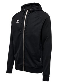 Hoodie zippé noir en tissu doux, avec une fermeture éclair blanche, des poches latérales, des poignets côtelés, et un petit logo sur la poitrine.