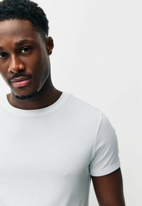 Tričko s krátkym rukávom, priliehavé, vyrobené z ľahkého sivého materiálu. Hladká textúra, okrúhly výstrih, minimalistický dizajn. Žiadne viditeľné vzory ani logá.