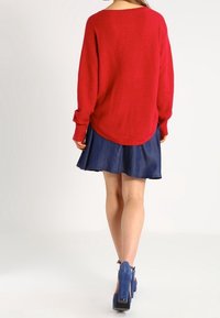 Rode, gestructureerde trui met een losse fit, gecombineerd met een blauwe spijkerrok. De outfit heeft een relaxte halslijn en korte mouwen.