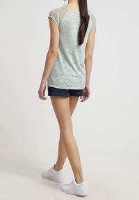 Top de manga corta en verde menta claro con tejido texturizado y hombros de malla con puntos, combinado con shorts de mezclilla oscura y zapatillas blancas.