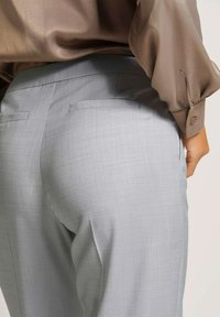  Lichtgrijze, op maat gemaakte broeken met een gladde textuur, voorzien van achterzakken en een slimfit ontwerp, gecombineerd met een licht glanzende bruine blouse.