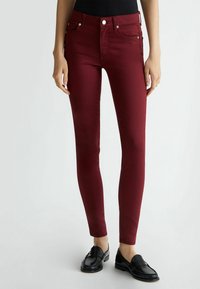 Bordowe obcisłe dżinsy z wysokim stanem, szlufkami na pasek i przednimi kieszeniami. Zestawione z czarnymi mokasynami. Gładka faktura.
