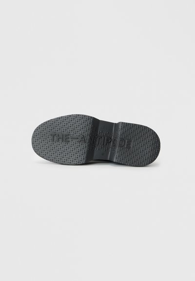 Semelle de chaussure en caoutchouc noir avec un motif texturé et une marque. La forme est arrondie avec une finition lisse et une large zone de talon.