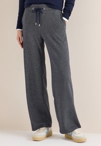 Szare, szerokie spodnie dresowe z elastycznym pasem i sznurkami zakończonymi srebrnymi końcówkami. Miękki materiał, boczne kieszenie, noszone z jasnymi sneakersami.