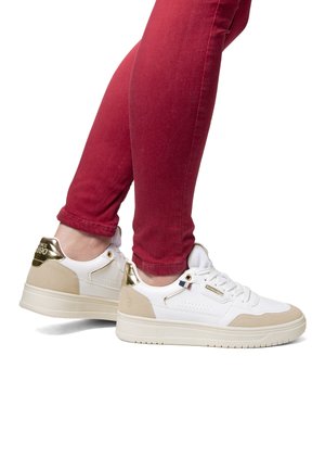 Hvide sneakers med beige accenter og en guldfarvet hælflap. De har et glat læderoverdel, perforeret design og tykke gummisåler.